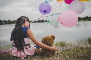 liten flicka med en nallebjörn och ballonger på ängfältet foto