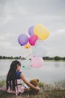 liten flicka med en nallebjörn och ballonger på ängfältet foto