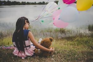 liten flicka med en nallebjörn och ballonger på ängfältet