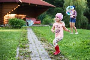 Lycklig flicka spelar med tvål bubblor utomhus. en liten flicka poppar en tvål bubbla foto
