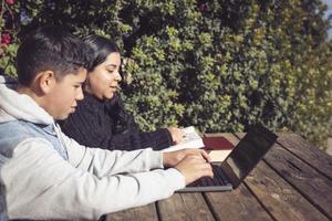 två ung latino studenter, utomhus, använder sig av bärbara datorer, Sammanträde på en parkera foto