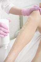 kosmetolog applicering guide gel på klientens ben. ipl laser epilering procedur. få slät hud i en salong. vertikal storlek foto