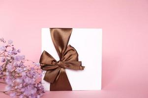 en gåva kuvert med en rosett, med ett tömma kopia Plats på en rosa bakgrund. platt står. Gypsophila blommor foto