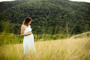 ung gravid kvinna som kopplar av utanför i naturen