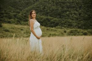 ung gravid kvinna som kopplar av utanför i naturen