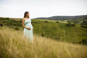 ung gravid kvinna som kopplar av utanför i naturen foto