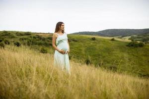 ung gravid kvinna som kopplar av utanför i naturen foto