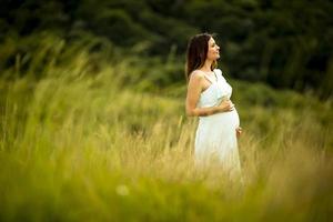 ung gravid kvinna som kopplar av utanför i naturen foto