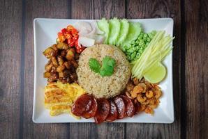 ris kryddat med räkorpasta, med rödlök, bönor, mango och stekt ägg på vit platta på träbord