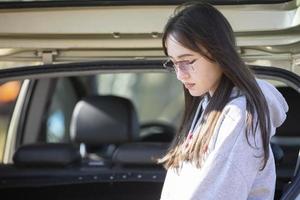 en skön flicka med lång hår och glasögon på de bakgrund av ett öppen bil trunk. foto