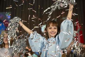 Lycklig liten flicka i konfetti.magi tid - porträtt av en mycket Lycklig barn med händer leende medan faller konfetti. på en barns fest eller födelsedag. foto
