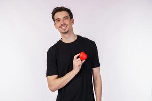 porträtt av Lycklig ung caucasian man bär svart t-shirt är innehav en röd äpple på isolerat bakgrund foto