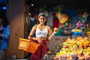 ung kvinna do handla i mataffär. välja äpplen i Lagra foto