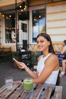 leende kvinna innehav telefon utomhus i Kafé. foto