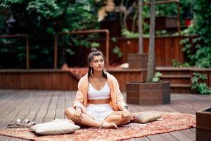 ung kvinna är praktiserande yoga Sammanträde på en trä- podium foto