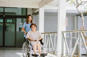 leende sjukgymnast tar hand om den glada äldre patienten i rullstol foto