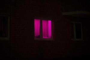 reste sig fönster på natt. rosa ljus i hus. foto