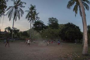 gili asahan, indonesien - augusti, 22 2016 - Pojkar är spelar fotboll på solnedgång på en handflatan träd fält nära de strand foto