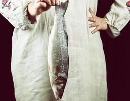 kvinna i grå Linné kläder innehav en färsk hav bas fisk foto