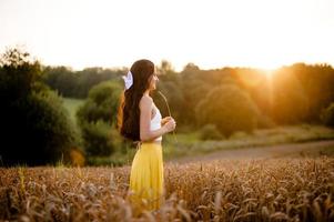 en flicka med lång hår står i en gul kjol i en fält med spikelets och utseende på de Sol foto