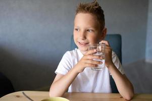 en söt pojke drycker vatten och äter en torr frukost på Hem och ler foto