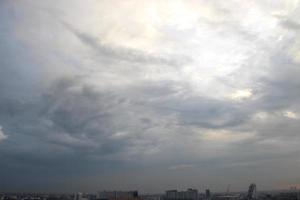 solnedgång himmel ovan tung mörk moln nästan regnar med dramatisk strålar av ljus lysande ner bakgrund och stad kväll tid foto