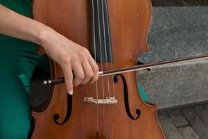 detalj av en man spelar de trä- cello gnuggning de strängar med de rosett till skaffa sig de anteckningar av en klassisk musik bit. foto
