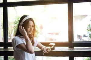 ung kvinna lyssnar på musik i hörlurar med fönsterbrädan bakgrund. foto