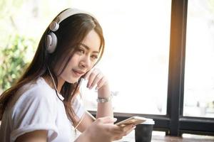 ung kvinna lyssnar på musik i hörlurar med fönsterbrädan bakgrund. foto