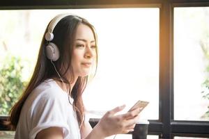 ung kvinna lyssnar på musik i hörlurar med fönsterbrädan bakgrund foto