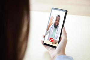 kvinna patient innehar en svart smartphone chattar uppkopplad med ett afrikansk amerikan manlig läkare. begrepp av uppkopplad kommunikation teknologi. doktorer kan undersöka patienter genom video samtal. klippning klappa foto
