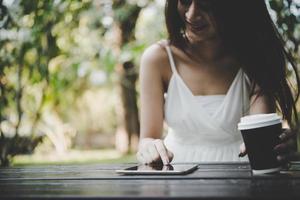 ung kvinna som håller engångskaffe kopp medan textmeddelanden genom smartphone utomhus foto