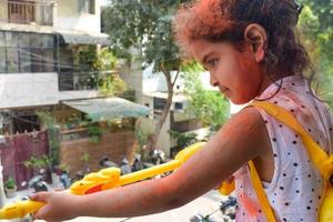 ljuv liten indisk flicka spelar färger på holi festival, innehav pichakaree full av färger, holi festival fester i delhi, Indien foto