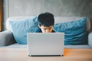 fyra år gammal pojke asiatisk man sitter på en skärm medan studerar på en kaffe affär använder sig av hans bärbar dator till studie uppkopplad under de covid-19 nedstängning. uppkopplad utbildning, hemskola. foto