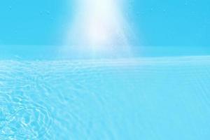 defokusering suddig transparent blå färgad klar lugna vatten yta textur med stänk och bubblor. trendig abstrakt natur bakgrund. vatten vågor i solljus med kopia Plats. blå vatten glans foto