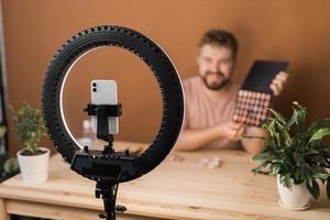 manlig skönhet bloggare med smink produkt inspelning video på Hem. använder sig av ringa lampa och smartphone. vlog kosmetisk Produkter och mångfald begrepp foto