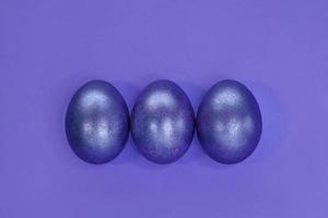 tre 3 påsk ägg färgad skinande mycket peri trendig Färg lagd ut i ett linje på violett papper bakgrund. glitter måla för ägg. hälsningar kort för påsk Semester. plats för text. foto
