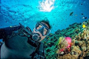 rolig dykning dykare selfie i blå hav bakgrundsbelysning Sol med clown fisk inuti anemon foto