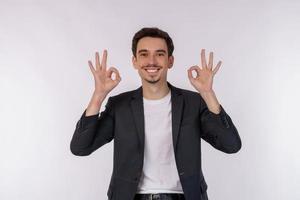 porträtt av Lycklig ung stilig affärsman håller på med ok tecken med hand och fingrar över vit bakgrund foto