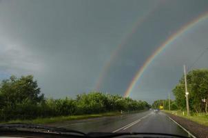 se av de väg från de bil fönster, där är en regnbåge i de himmel foto