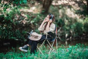 ung asiatisk kvinna Sammanträde på stol lyssnande musik från hörlurar foto