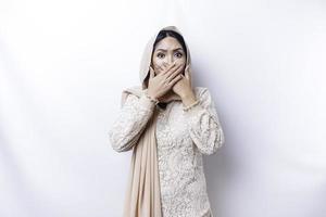 hoppsan överraskad ung asiatisk muslim kvinna beläggning mun med händer och stirrande på kamera medan stående mot vit bakgrund foto