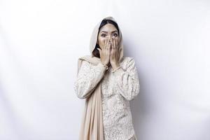 hoppsan överraskad ung asiatisk muslim kvinna beläggning mun med händer och stirrande på kamera medan stående mot vit bakgrund foto