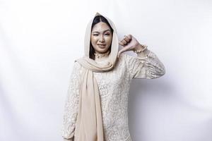 besviken asiatisk muslim kvinna bär en hijab ger tummen ner hand gest av ogillande, isolerat förbi vit bakgrund foto