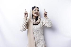upphetsad asiatisk muslim kvinna bär hijab pekande på de kopia Plats ovan henne, isolerat förbi vit bakgrund foto
