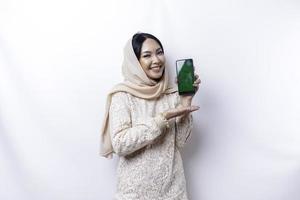 en porträtt av en Lycklig asiatisk muslim kvinna bär en hijab, som visar henne telefon skärm, isolerat förbi vit bakgrund foto