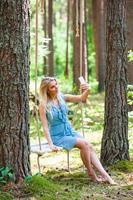 skön blond kvinna i blå klänning använder sig av smartphone till tar selfie foto