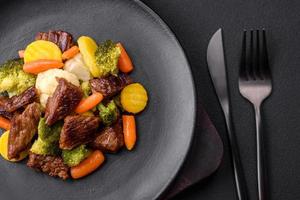 utsökt färsk nötkött och grönsaker morötter, broccoli, blomkål på en svart tallrik foto