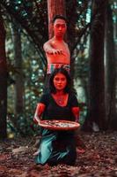 ett asiatisk kvinna och man var stående i främre av en träd medan jakt ett djur- i de mitten av de skog fram tills de var täckt i blod foto