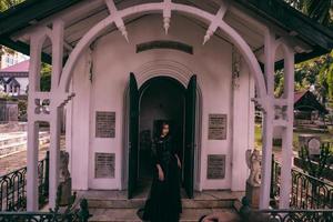 en häxa i ett Allt svart klänning och skrämmande smink var stående på de kyrkogård Port foto